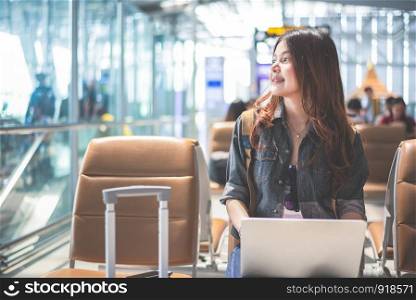 Beauty Asian woman using laptop and looking outside at airport. Woman sitting in airport terminal. People and lifestyle concept. Technology and travel theme. Business and Portrait theme.