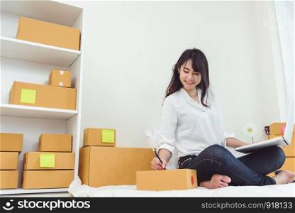 Beauty Asian woman using laptop and start up small business entrepreneur SME and checking order list in bedroom, Young happy freelance woman shopping online marketing or sending parcel to customers
