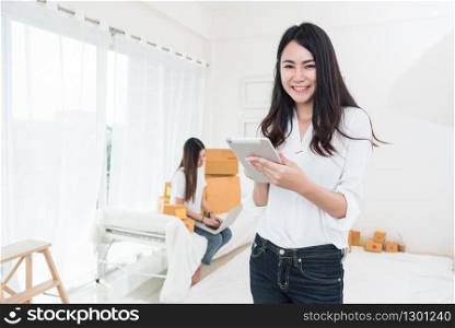 Beauty Asian woman using tablet for checking order from customers at home. Business and Delivery transportation concept. Logistic service and Product packing theme. Girl looking at camera