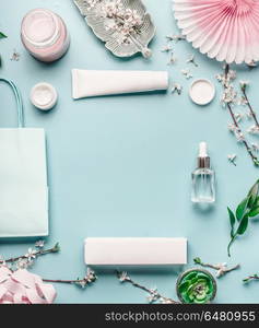 Beauty background with facial cosmetic products, shopping bag and twigs with cherry blossom on pastel blue desktop background. Spring skin care trends, top view, frame, flat lay. Branding mock up