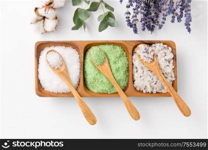 beauty, bath and wellness concept - sea salt with lavender, eucalyptus cinerea, cotton flowers and spoons on wooden tray. sea salt with wooden spoons and herbs