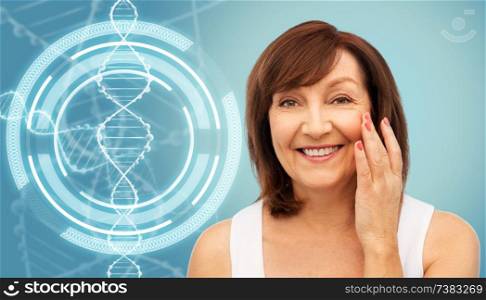 beauty, biotechnology and anti-age concept - portrait of smiling senior woman touching her face over blue background and dna molecule hologram. senior woman touching her face over dna molecule