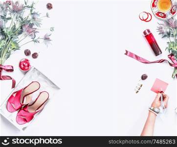 Beauty blog background. New shoes in a box, woman hand with bracelets writes a note, flowers bunch with ribbon, cosmetic and perfume, jewelry , cup of tea on white desktop. Top view. Fashion blogging