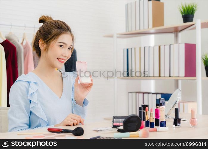 Beauty blogger present beauty cosmetics sitting in front camera for recording video. Beautiful asian woman use cosmetics while review make up tutorial broadcast live video to social network by internet.
