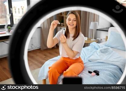 beauty blogging, make up and people concept - happy smiling girl blogger with ring light and smartphone applying mascara at home. girl blogger with ring light applying make up