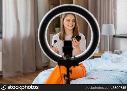 beauty blogging, technology and people concept - happy smiling girl blogger with ring light and smartphone applying make up at home. girl blogger with ring light applying make up
