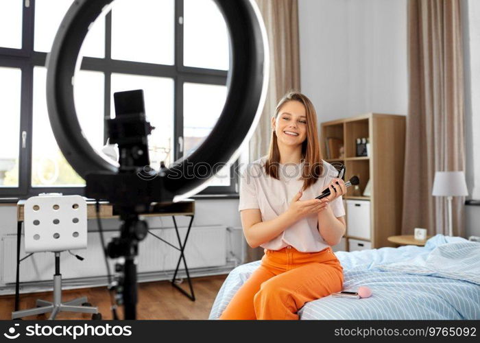 beauty blogging, technology and people concept - happy smiling girl blogger with ring light and smartphone applying make up at home. girl blogger with ring light applying make up