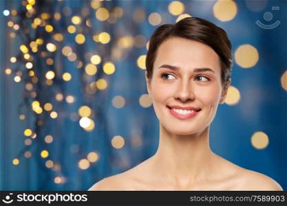 beauty, bodycare and people concept - beautiful smiling young woman with bare shoulder over holidays lights on dark blue background. beautiful smiling young woman with bare shoulder