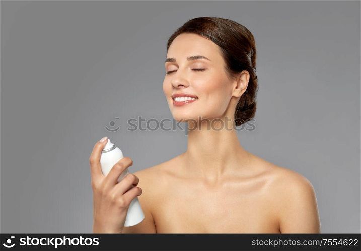 beauty, bodycare and people concept - beautiful young woman applying facial spray or mist to her face skin over grey background. beautiful young woman with facial spray or mist