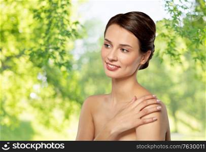 beauty, bodycare and people concept - beautiful young woman touching her bare shoulder over green natural background. beautiful young woman touching bare shoulder