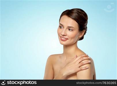 beauty, bodycare and people concept - beautiful young woman touching her bare shoulder over blue background. beautiful young woman touching bare shoulder