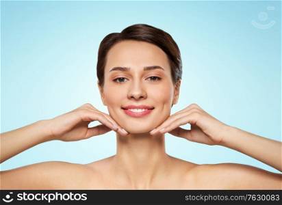beauty, bodycare and people concept - beautiful young woman touching her face and chin over blue background. beautiful young woman touching her face and chin