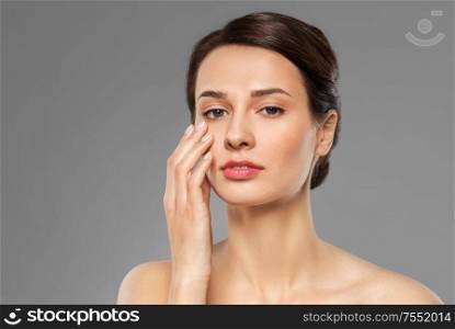 beauty, bodycare and people concept - beautiful young woman touching her face over grey background. beautiful young woman touching her face