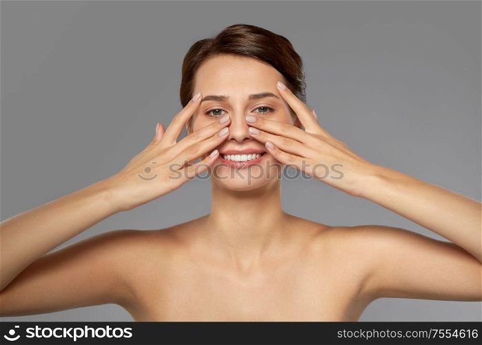 beauty, bodycare and people concept - beautiful young woman touching her face over grey background. beautiful young woman touching her face