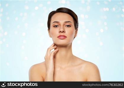 beauty, bodycare and people concept - beautiful young woman touching her neck over lights on blue background. beautiful young woman touching her neck
