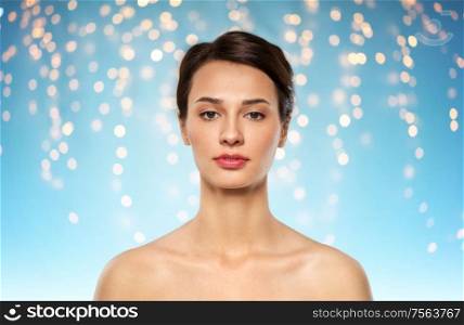 beauty, bodycare and people concept - beautiful young woman with bare shoulder over holidays lights on blue background. beautiful young woman with bare shoulder