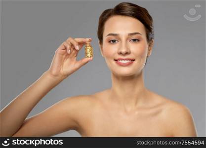 beauty, bodycare and people concept - beautiful young woman with gold facial mask in bottle over grey background. beautiful young woman with gold facial mask