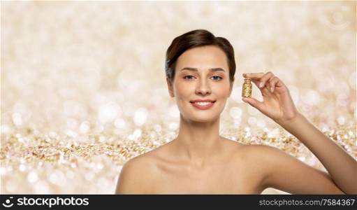 beauty, bodycare and people concept - beautiful young woman with gold facial mask in bottle over shimmering golden glitter on background. beautiful young woman with gold facial mask