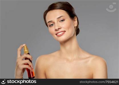 beauty, bodycare and people concept - beautiful young woman with sun protective oil over grey background. beautiful young woman with sun protective oil