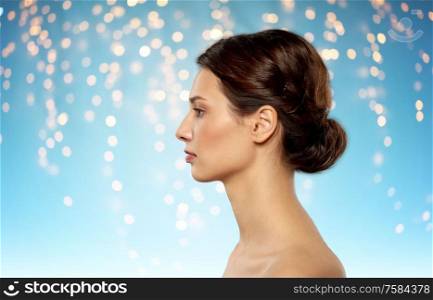 beauty, bodycare and people concept - profile of beautiful young woman with bare shoulders over holidays lights on blue background. profile of beautiful woman with bare shoulders