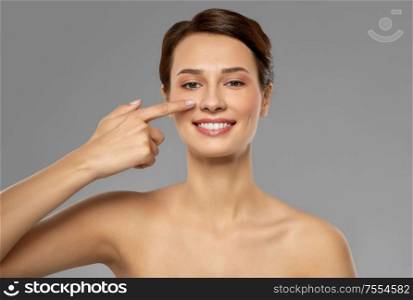 beauty, bodycare and people concept - smiling beautiful young woman showing her nose over grey background. beautiful smiling woman showing her nose