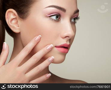 Beauty brunette woman with perfect makeup. Pink lips and nails. Perfect eyebrows. Skin care foundation. Beauty girls face isolated on beige background. Hands with beautiful elegant manicure