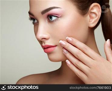 Beauty brunette woman with perfect makeup. Pink lips and nails. Perfect eyebrows. Skin care foundation. Beauty girls face isolated on beige background. Hands with beautiful elegant manicure