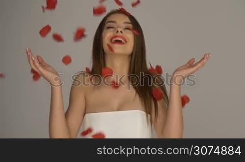 Beauty brunette woman with rose petals falling down wearing white dress