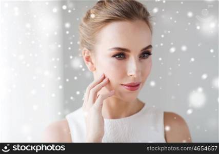 beauty, christmas, holidays and people concept - close up of beautiful smiling woman in white dress touching her face over snow