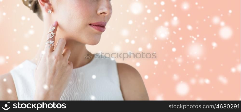 beauty, christmas, holidays, people and luxury concept - close up of beautiful woman with golden ring and diamond earring over beige background and snow