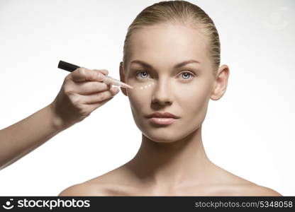 beauty close-up portrait of cute blonde girl with tied back hair applying cosmetics on her perfect natural skin. Preparing for make-up