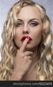 beauty close-up portrait of pretty blonde girl with wavy shiny hair, red lipstick and nail polish. Sensual pose