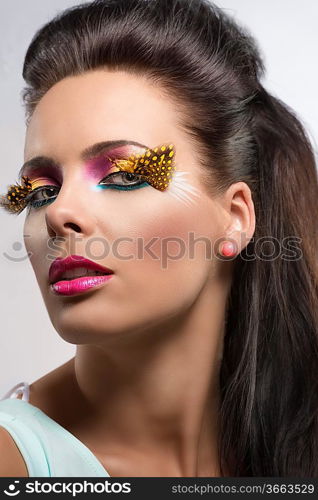 beauty close-up portrait with colored and feathered make up, she is turned at right and looks in to the lens