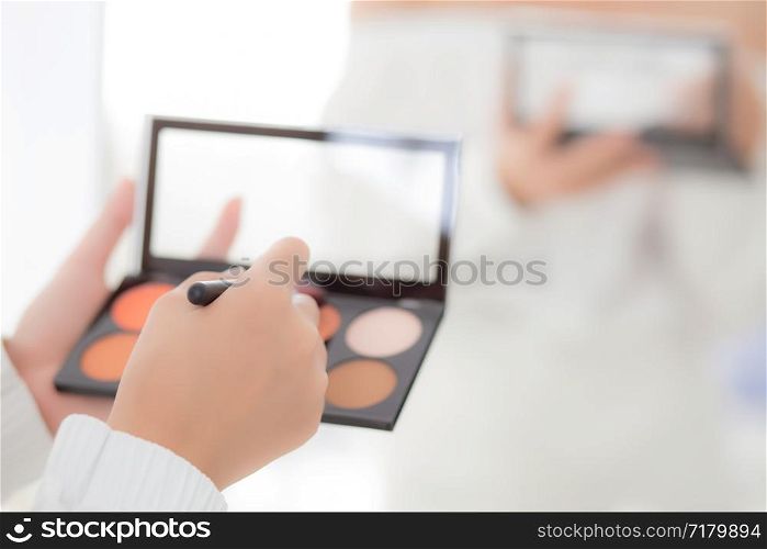 Beauty closeup young asian woman with back view applying makeup with brush cheek on hand, beautiful girl holding blusher rear view, skin care and cosmetic table fashion concept.