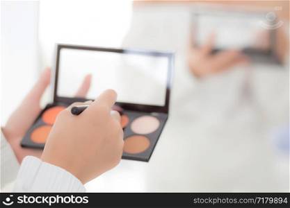 Beauty closeup young asian woman with back view applying makeup with brush cheek on hand, beautiful girl holding blusher rear view, skin care and cosmetic table fashion concept.