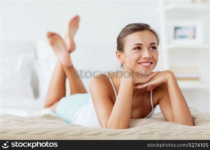 beauty, comfort and people concept - beautiful happy young woman lying on bed at home bedroom. beautiful happy young woman lying on bed at home