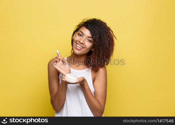 Beauty Concept - Beautiful young African American woman happy using skin care cream. Yellow studio background. Copy Space.. Beauty Concept - Beautiful young African American woman happy using skin care cream. Yellow studio background. Copy Space