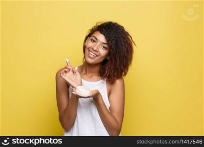 Beauty Concept - Beautiful young African American woman happy using skin care cream. Yellow studio background. Copy Space.. Beauty Concept - Beautiful young African American woman happy using skin care cream. Yellow studio background. Copy Space
