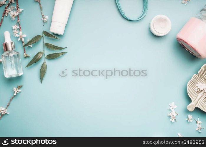 Beauty concept with facial cosmetic products, green leaves and cherry blossom on pastel blue desktop background. Modern skin care layout, top view, frame, flat lay. Branding mock up