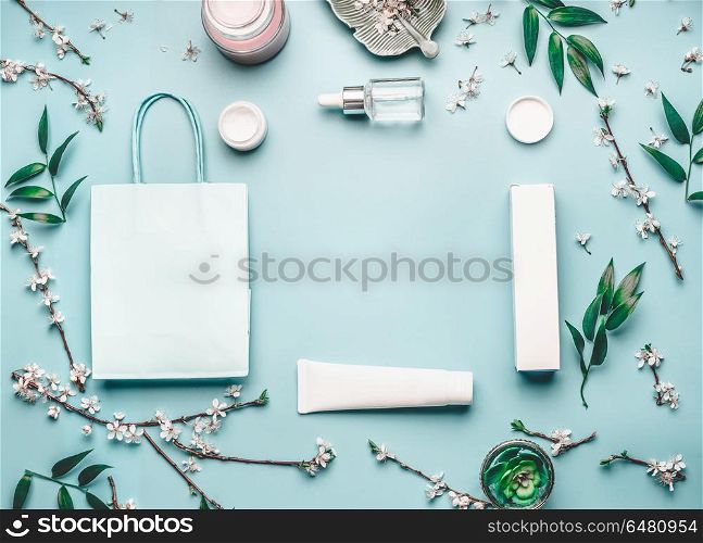 Beauty concept with facial cosmetic products, shopping bag and cherry blossom on pastel blue desktop background. Modern spring skin care layout, top view, frame, flat lay. Branding mock up