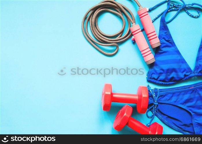 Beauty concept with sport equipments and blue color bikini on blue background, Flat lay healthy concept