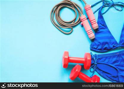 Beauty concept with sport equipments and blue color bikini on blue background, Flat lay healthy concept