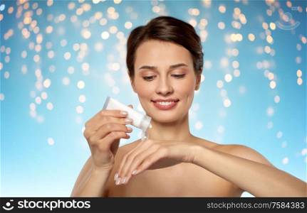 beauty, cosmetics and bodycare concept - beautiful woman applying moisturizing cream to her hand over holidays lights on blue background. woman applying moisturizing cream to her hand
