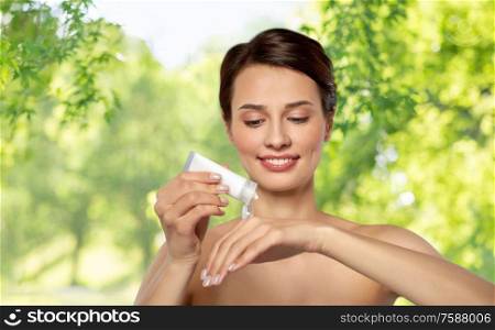 beauty, cosmetics and bodycare concept - beautiful woman applying moisturizing cream to her hand over green natural background. woman applying moisturizing cream to her hand