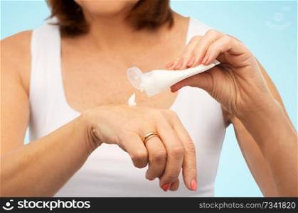 beauty, cosmetics and bodycare concept - close up of senior woman applying hand cream over blue background. close up of senior woman applying hand cream