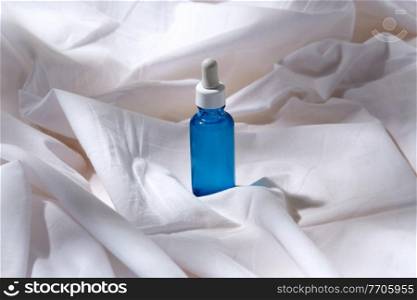beauty, cosmetics and object concept - bottle of serum on white sheet with folds. bottle of serum on white sheet
