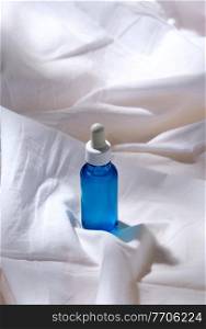 beauty, cosmetics and object concept - bottle of serum on white sheet with folds. bottle of serum on white sheet