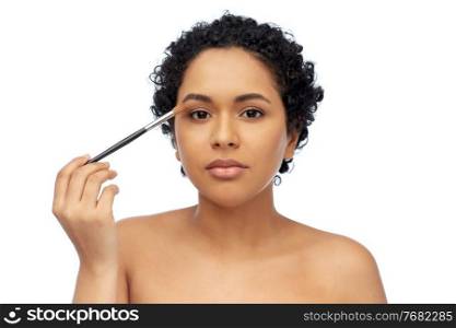 beauty, cosmetics and people concept - beautiful young african american woman with make up brush applying eye shadows over white background. african american woman with make up brush
