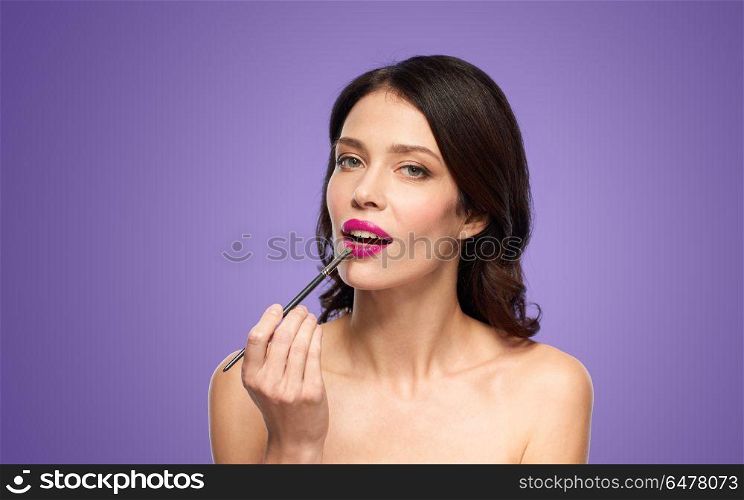 beauty, cosmetics and people concept - beautiful young woman with make up brush applying pink lipstick over ultra violet background. beautiful woman with make up brush for lipstick. beautiful woman with make up brush for lipstick