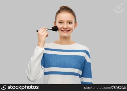 beauty, cosmetics and people concept - happy smiling teenage girl in pullover with make up brush over grey background. happy smiling teenage girl with make up brush